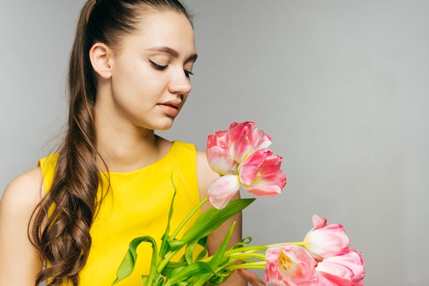 Linda garota com um vestido amarelo segurando um grande buquê de flores cor de rosa, comemora