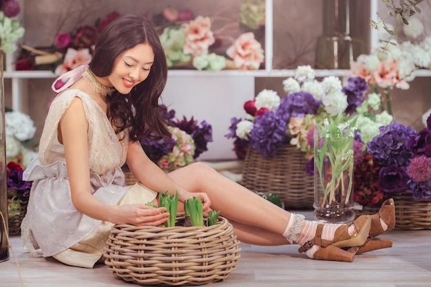 Linda garota com um vestido branco macio sentada no chão contra flores