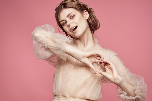 Linda garota com um vestido delicado, posando em um fundo rosa e sorrindo