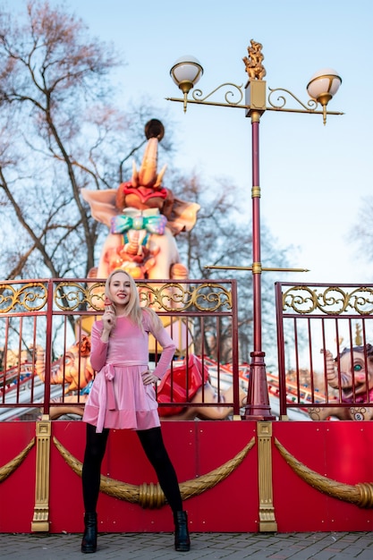 Foto linda garota com um vestido rosa andando no parque de diversões