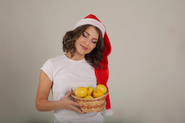 linda garota com uma camiseta branca e um chapéu de Papai Noel segurando uma cesta de limões nas mãos