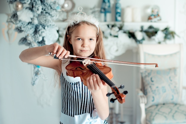 Linda garota com violino na sala de decoração de natal.