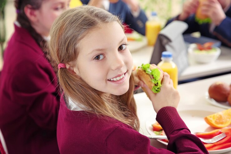 Foto linda garota comendo comida deliciosa enquanto está sentado na mesa de jantar no refeitório da escola