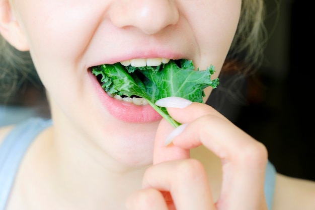 Foto linda garota comendo couve. a boca e os dentes são visíveis. superalimento.