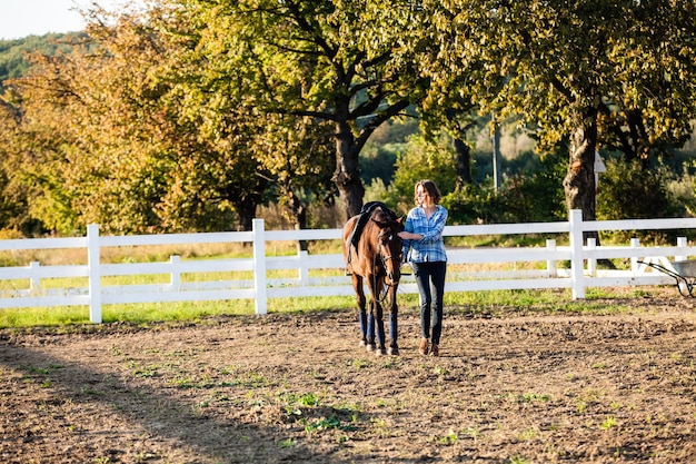 Linda garota conduzindo seu cavalo marrom na fazenda