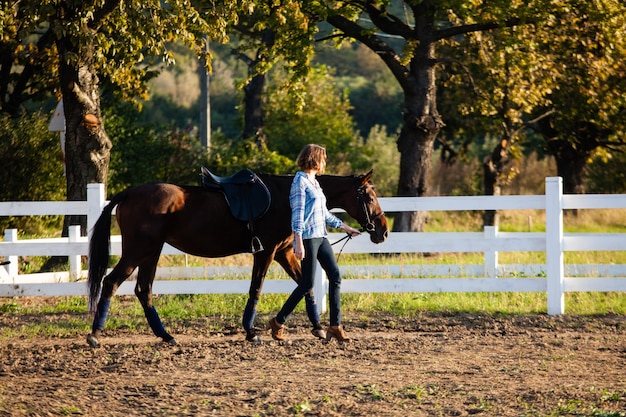 Linda garota conduzindo seu cavalo marrom na fazenda