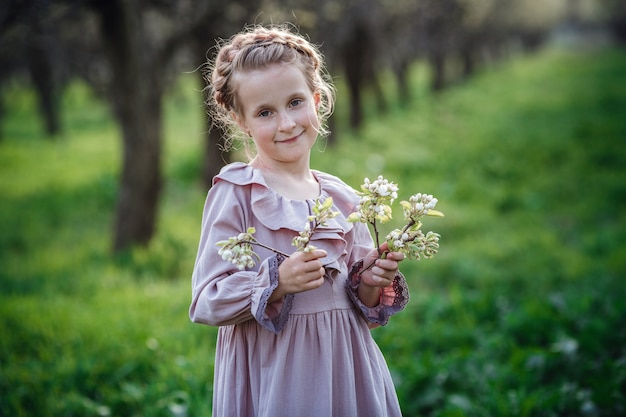 Linda garota de 6 a 7 anos de idade, posando no jardim. Páscoa. gosta de primavera e calor. Belo jardim de primavera. Conceito de infância, paz e felicidade feliz. Flor aromática e vintage retrô.