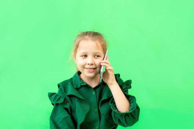 Linda garota de 7 a 9 anos falando ao telefone no verde