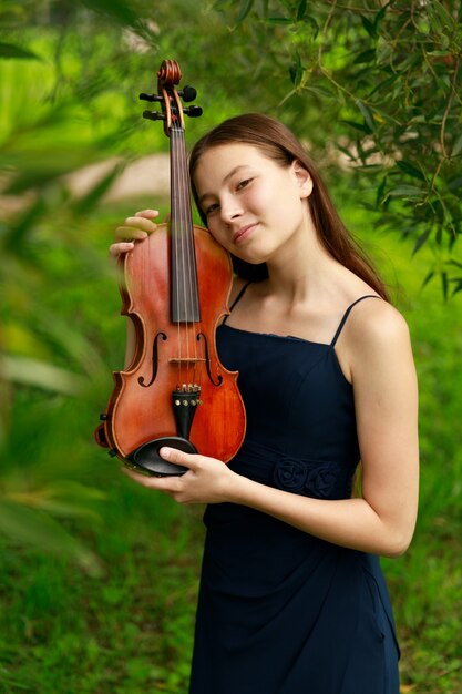 Linda garota de cabelos castanhos de aparência asiática com um violino na natureza. músico por natureza. música clássica. Foto de alta qualidade