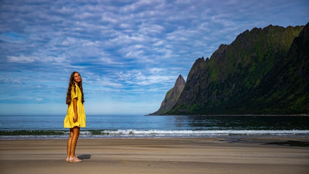 linda garota de cabelos compridos de vestido amarelo caminha na famosa praia ersfjordstranda, senja, noruega