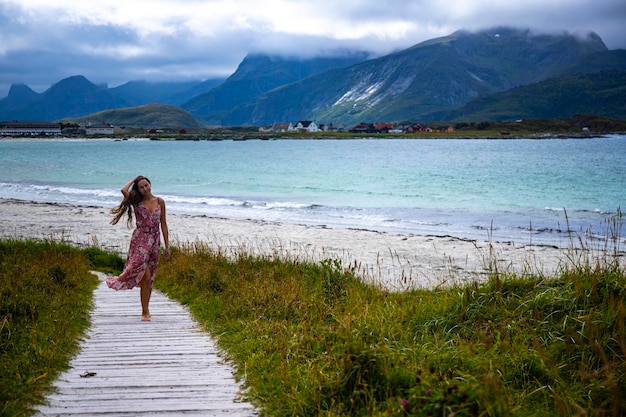 Linda garota de cabelos compridos em um vestido caminha ao longo da famosa praia de ramberg (rambergstranda), noruega