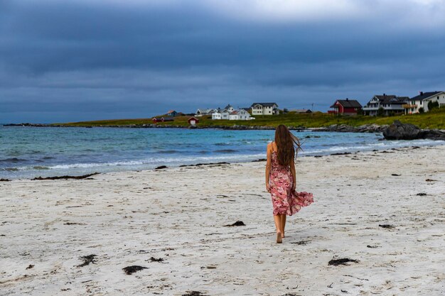 linda garota de cabelos compridos em um vestido caminha ao longo da famosa praia de ramberg (rambergstranda), noruega