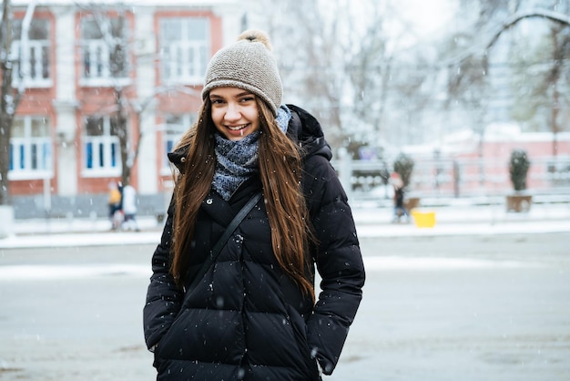 Linda garota de cabelos compridos em uma jaqueta quente andando pelas ruas da cidade no inverno sorrindo