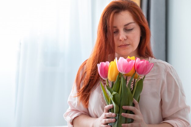 Linda garota de cabelos compridos, segurando um buquê de flores frescas tulipas na sala. Sorria no rosto, dia dos namorados, conceito de aniversário