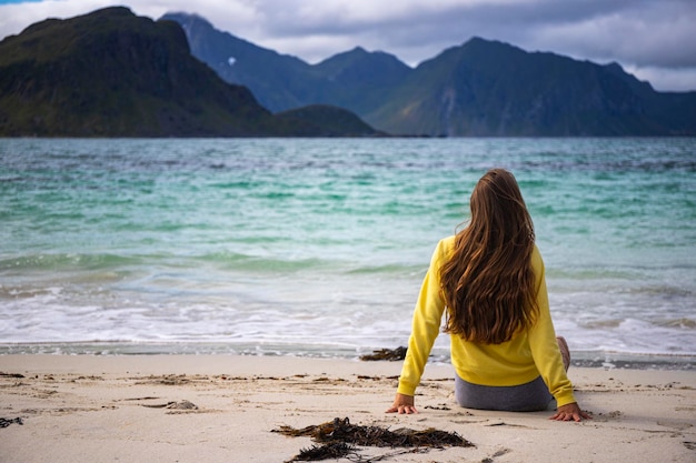 linda garota de cabelos compridos toma sol enquanto está sentado na areia na famosa praia de haukland, noruega