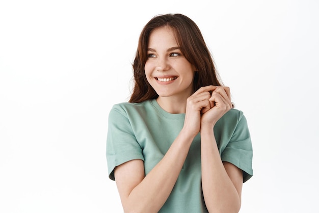 Linda garota de camiseta parecendo feliz de lado no texto promocional em pé alegre em camiseta casual com maquiagem natural nua no rosto fundo branco