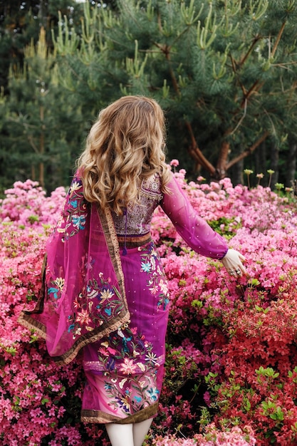 Foto linda garota de costas para a câmera em um sári rosa em um jardim de azaléia florescendo