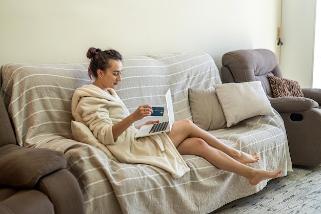 Linda garota de jaleco branco com um laptop de joelhos fazendo compras online em sites