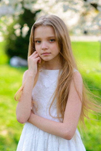 Linda garota de olhos azuis, com longos cabelos loiros em um vestido branco andando no jardim. verão brilhante, foto emocional.