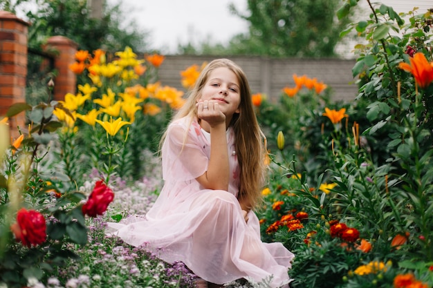 linda garota de olhos azuis, com longos cabelos loiros. menina em um vestido rosa flamingo. menina no jardim. verão brilhante, foto emocional. grande, grosso, brilhante jardim de flores perto de casa.