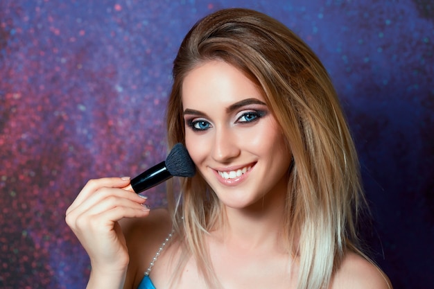 Linda garota de olhos azuis posando com borla para aplicar maquiagem