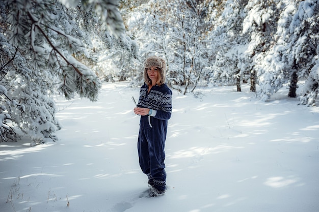 Linda garota de pé, no inverno no parque florestal, fundo de neve da árvore de Natal, ela está descansando no resort. Espaço livre para texto. Macacão azul para esportes.