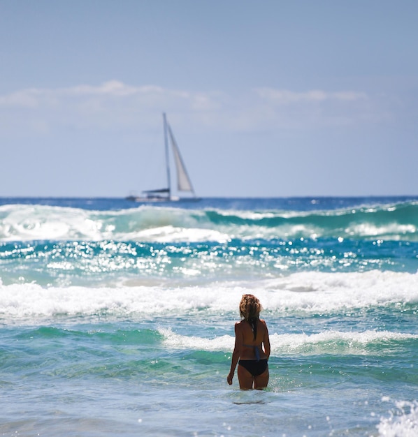 Linda garota de pé no mar azul Olha para o barco branco Oceano Pacífico