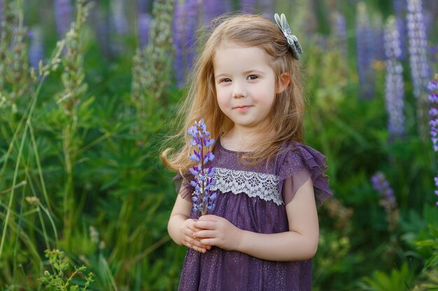 Linda garota de quatro anos com um vestido violeta segurando um buquê de flores de tremoço