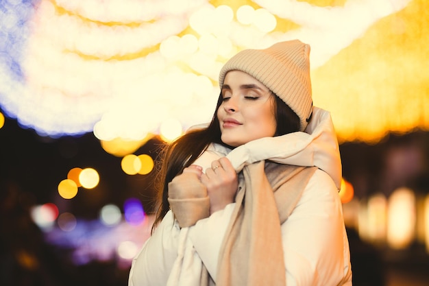 Linda garota de roupas quentes fica na rua e olha de lado contra o bokeh