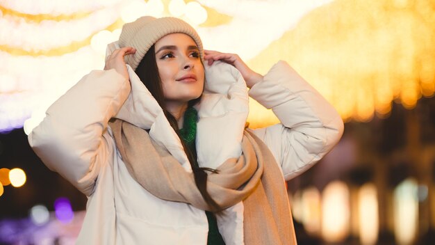 Linda garota de roupas quentes fica na rua e olha de lado contra o bokeh