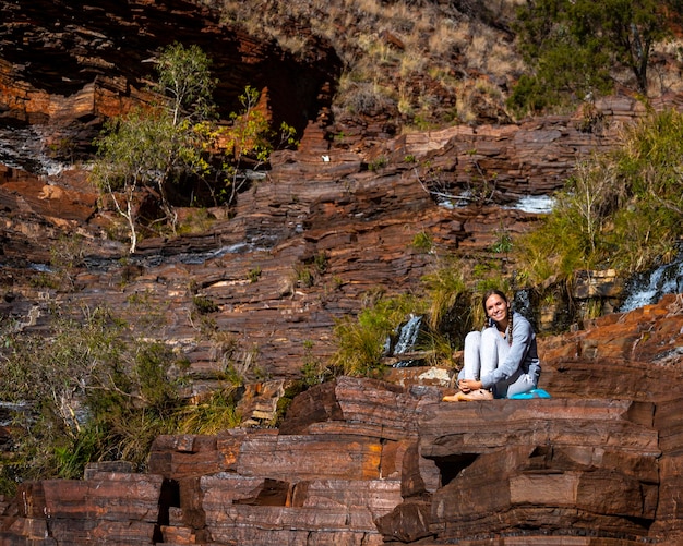 linda garota de tranças senta-se em camadas de pedras vermelhas no parque nacional karijini, na austrália ocidental