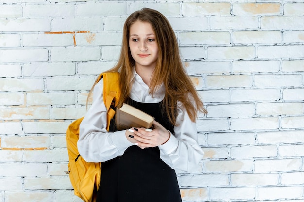 Linda garota de uniforme escolar segurando seu livro e pensando