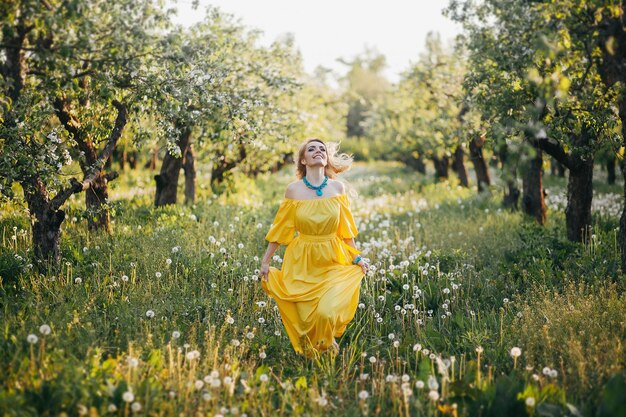 Linda garota de vestido amarelo no jardim florescendo