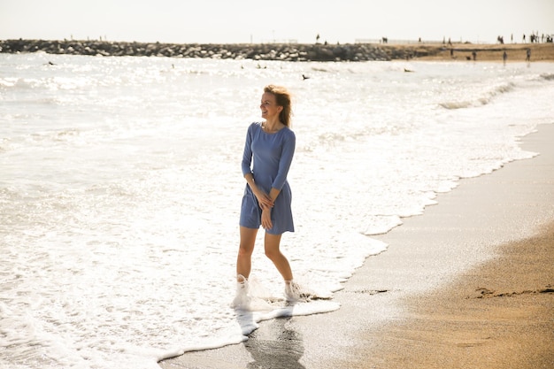 Linda garota de vestido azul está andando na praia Incrível foto de verão Mulher dançando e pulando perto do mar Emoções felizes e divertidas Conceito de viagem de férias Pernas finas Água morna do oceano