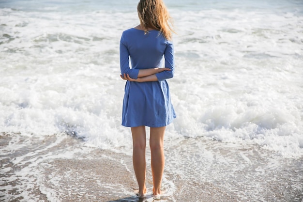 Linda garota de vestido azul está andando na praia Incrível foto de verão Mulher perto do mar Conceito de viagem de férias Pernas finas Água quente do oceano