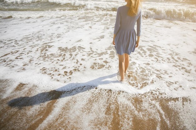 Linda garota de vestido azul está andando na praia Incrível foto de verão Mulher perto do mar Conceito de viagem de férias Pernas finas Água quente do oceano