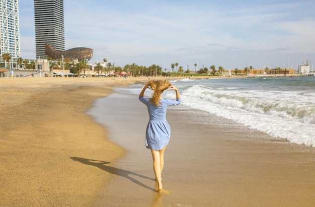 Linda garota de vestido azul está andando na praia Incrível foto de verão Mulher perto do mar Emoções felizes e divertidas Conceito de viagem de férias Pernas finas Água quente do oceano