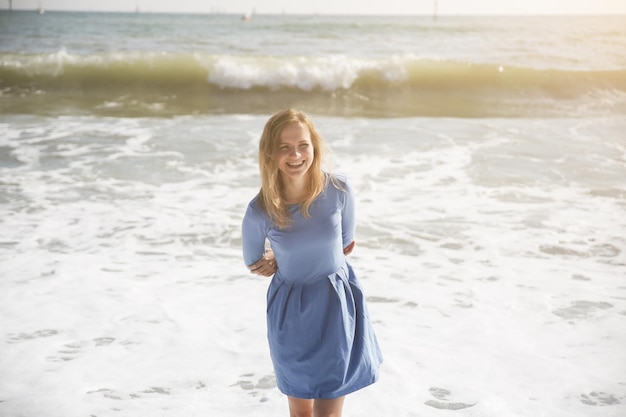 Linda garota de vestido azul está andando na praia Incrível foto de verão Mulher perto do mar Emoções felizes e divertidas Conceito de viagem de férias Pernas finas Água quente do oceano