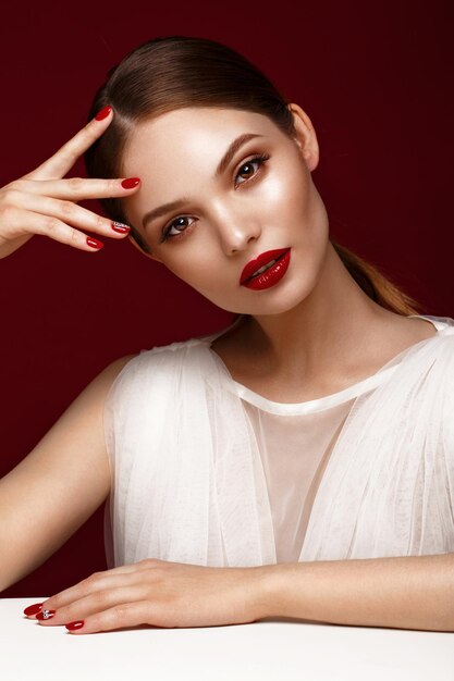 Linda garota de vestido branco com maquiagem clássica e manicure vermelha Rosto de beleza Foto tirada no estúdio