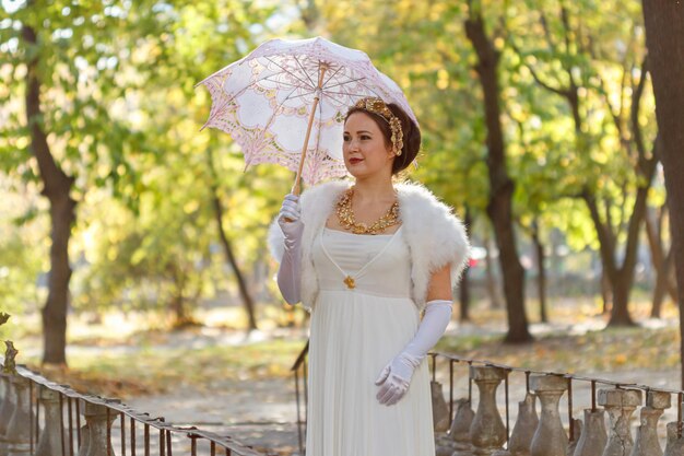 Linda garota de vestido branco com um guarda-chuva rosa em um fundo de árvores de outono