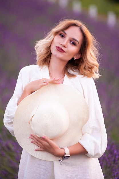 Linda garota de vestido branco e chapéu em um campo de lavanda ao pôr do sol