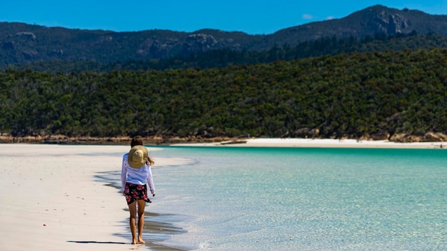 linda garota de vestido e camisa e chapéu caminha na praia whitehaven, ilha de whitsunday, austrália