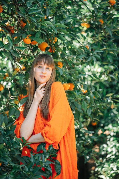 Linda garota de vestido laranja está olhando para longe segurando o dedo indicador sob o queixo no jardim laranja