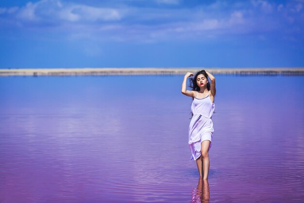 Linda garota de vestido longo branco posando no lago rosa salgado.