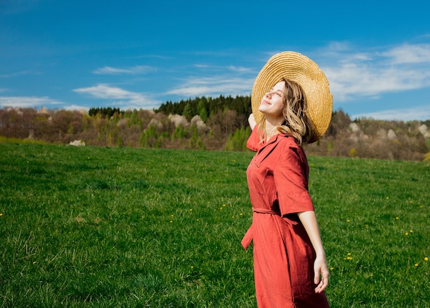 Linda garota de vestido vermelho e chapéu tem um tempo despreocupado no prado nas montanhas por uma floresta. temporada de primavera