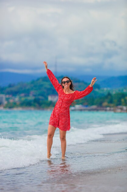 Linda garota de vestido vermelho na praia se divertindo