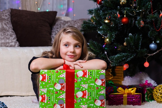 Linda garota deitada em uma caixa com um presente no fundo de uma árvore de Natal clima de Natal e ano novo