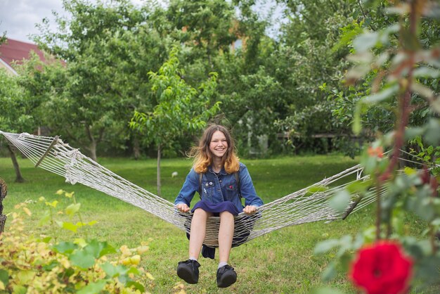 Linda garota deitada na rede, sorrindo e descansando adolescente no jardim primavera, copie o espaço