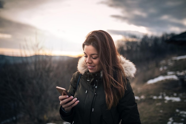 Linda garota desfrutando de uma caminhada na montanha e segurando seu celular