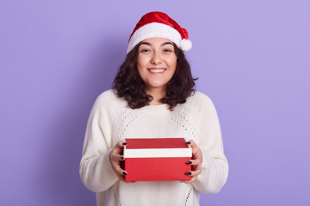 Linda garota do Papai Noel com presentes de Natal olhando diretamente para a câmera com um sorriso feliz